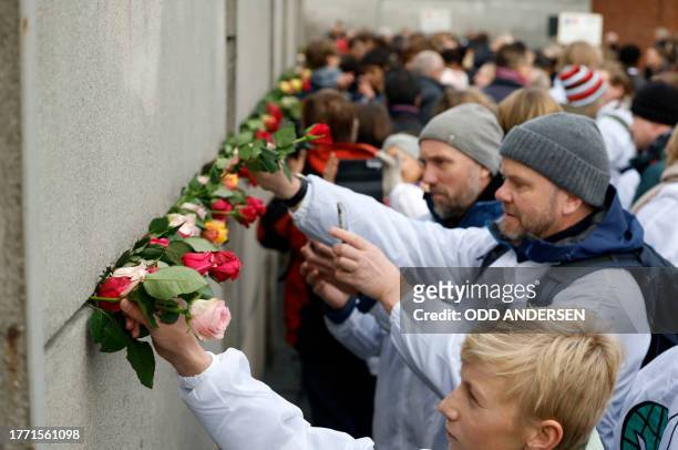 People place roses in the wall during festivities at the Berlin Wall Memorial, a 1,5 kilometers stretch on the former border strip between East and...