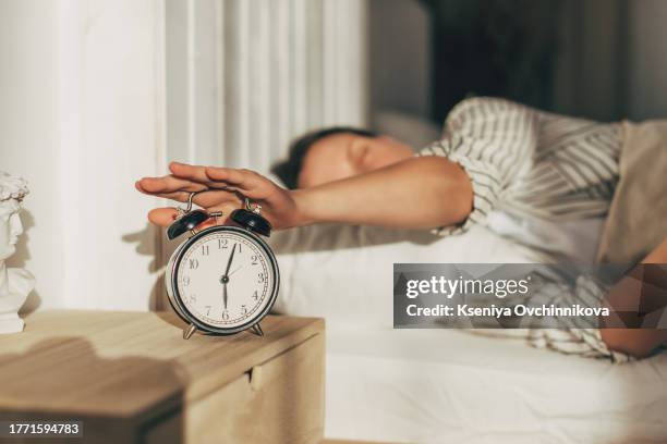 hand of woman turning off alarm clock on night table - time of day foto e immagini stock