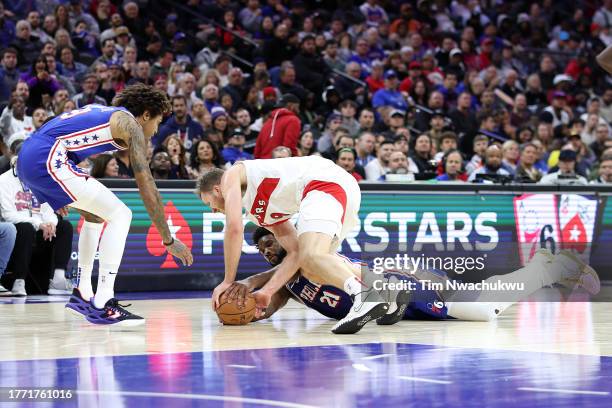 Jakob Poeltl of the Toronto Raptors challenges for the ball with Kelly Oubre Jr. #9 and Joel Embiid of the Philadelphia 76ers during the third...