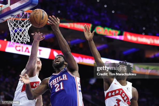 Joel Embiid of the Philadelphia 76ers challenges for the ball between Jakob Poeltl and O.G. Anunoby of the Toronto Raptors during the third quarter...