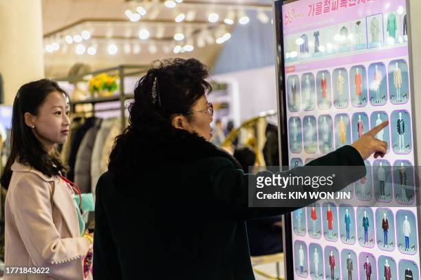 Visitors look at a display showing different clothing designs as they attend the opening of the 2023-Autumn Garment Exhibition at the Okryu...