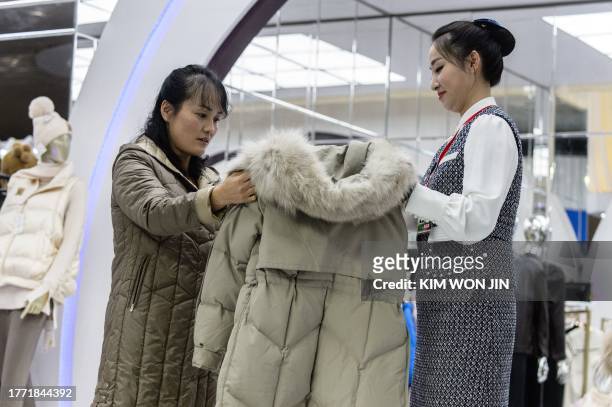 An assistant shows a woman a jacket during the opening of the 2023-Autumn Garment Exhibition at the Okryu Exhibition House in Pyongyang on November...