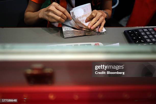 An employee counts Thai one-thousand baht banknotes at a Super Rich 1965 Co. Currency exchange store in Bangkok, Thailand, on Thursday, Aug. 22,...