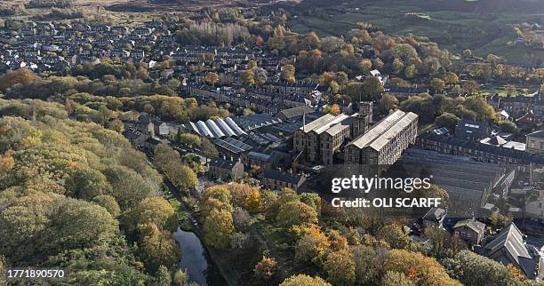 An overhead view shows deciduous trees bearing autumnal colours surrounding "New Mills", a derelict former textile mill in the village of Marsden,...