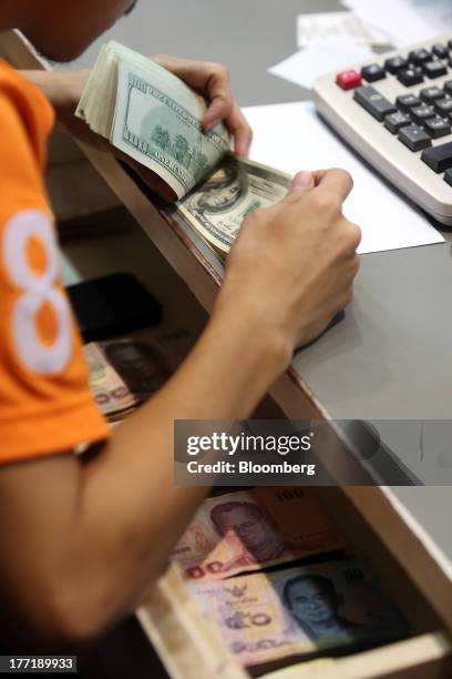 An employee counts U.S. One-hundred dollar banknotes as Thai baht banknotes sit inside a drawer at a Super Rich 1965 Co. Currency exchange store in...