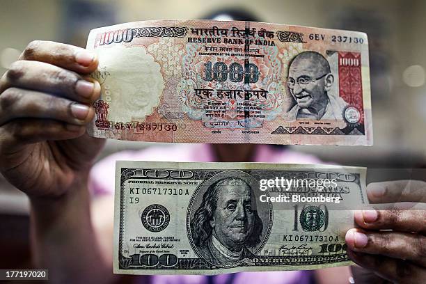 An employee displays an Indian one-thousand rupee banknote, top, and a U.S one-hundred dollar banknote for a photograph at a branch of the HDFC Bank...