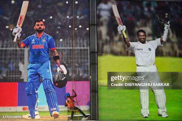 Worker fixes a poster of India's cricket player Virat Kohli alongside a poster of former player Sachin Tendulkar at the entrance of Eden Gardens...