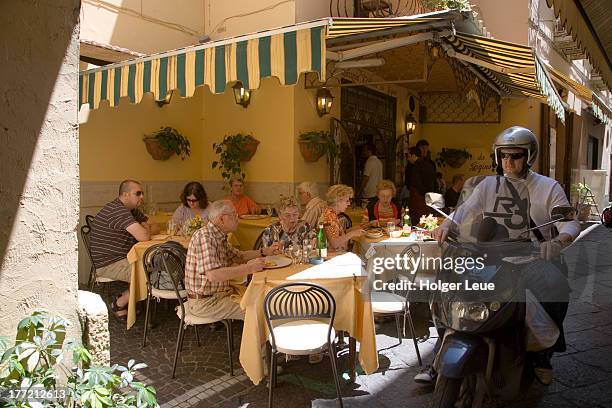 man on piaggio scooter rides past restaurant - sorrento stock pictures, royalty-free photos & images