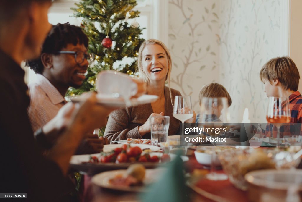 Smiling mature woman enjoying dinner with friends during Christmas at home