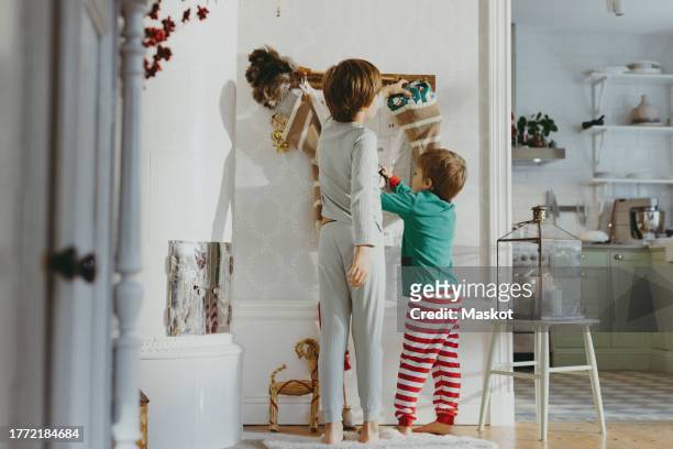 rear view of brothers removing gifts from stockings during christmas at home - kid stocking stock pictures, royalty-free photos & images