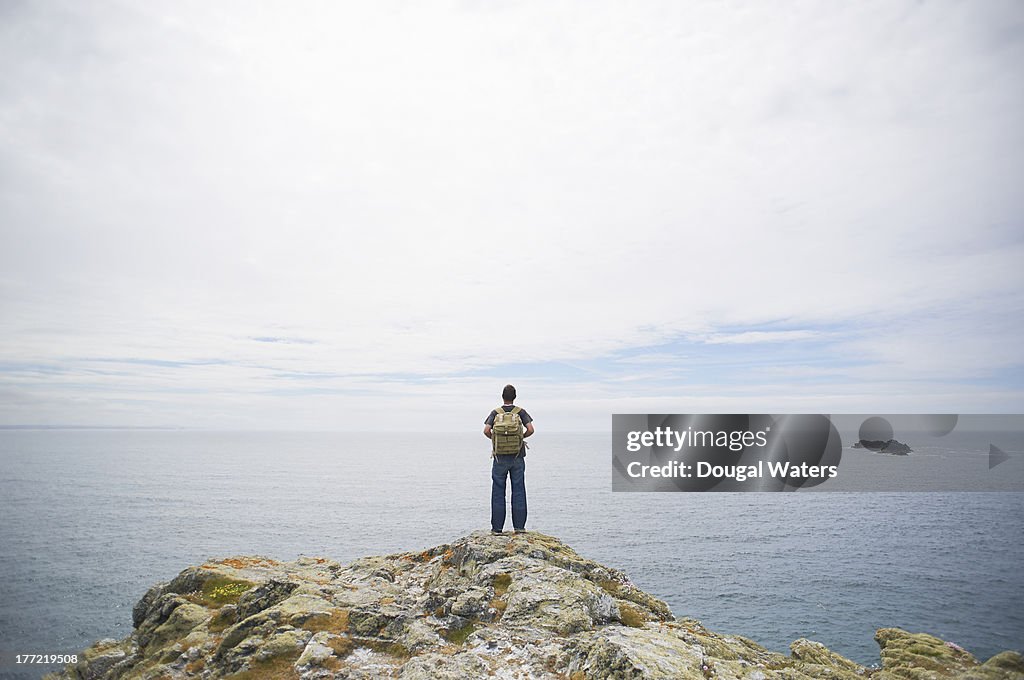 Hiker looking out to sea from cliff top.