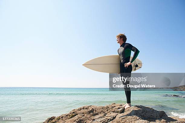 surfer with board standing on rocks. - surf board foto e immagini stock