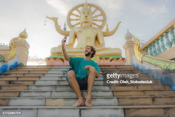 hombre fotografiando sentado en las escaleras en el templo del gran buda en ko samui - mobile sculpture fotografías e imágenes de stock