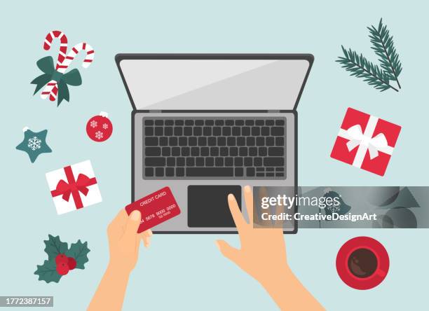 stockillustraties, clipart, cartoons en iconen met christmas online shopping concept with human hand holding credit card. high angle view of table with christmas decoration, gift boxes, candy canes and coffee cup - bovenop