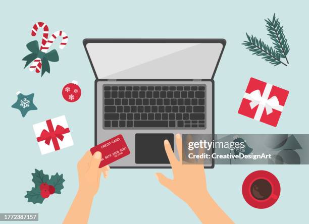christmas online shopping concept with human hand holding credit card. high angle view of table with christmas decoration, gift boxes, candy canes and coffee cup - christmas shopping stock illustrations