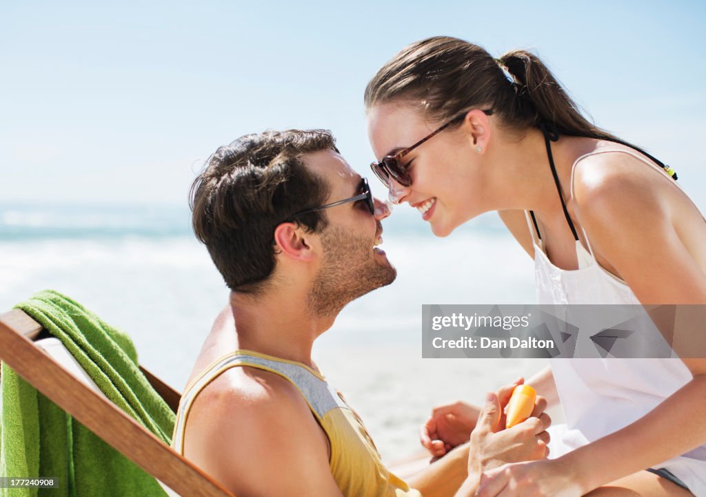 Happy couple rubbing sunscreen-covered noses on beach