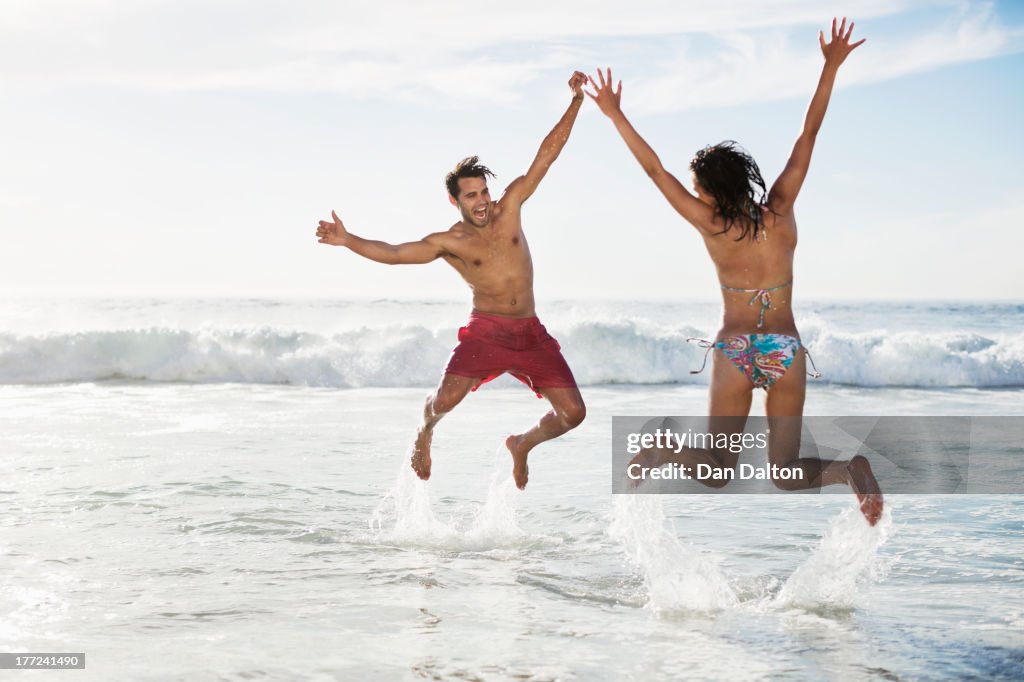 Coppia saltando con le braccia alzate sulla spiaggia
