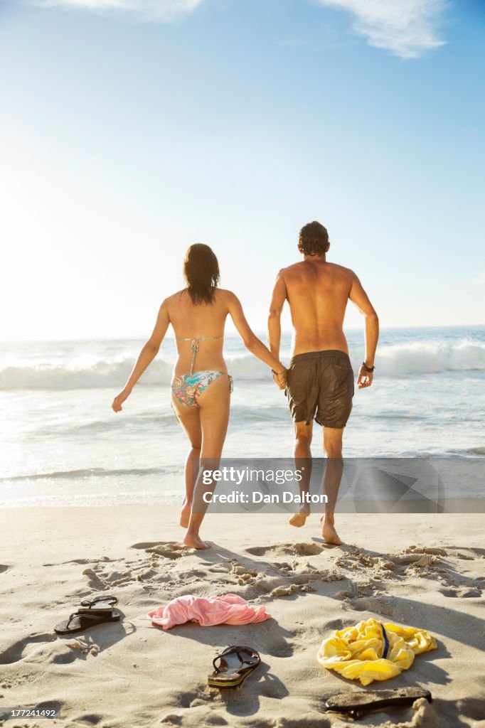 Couple holding hands and walking toward ocean on beach