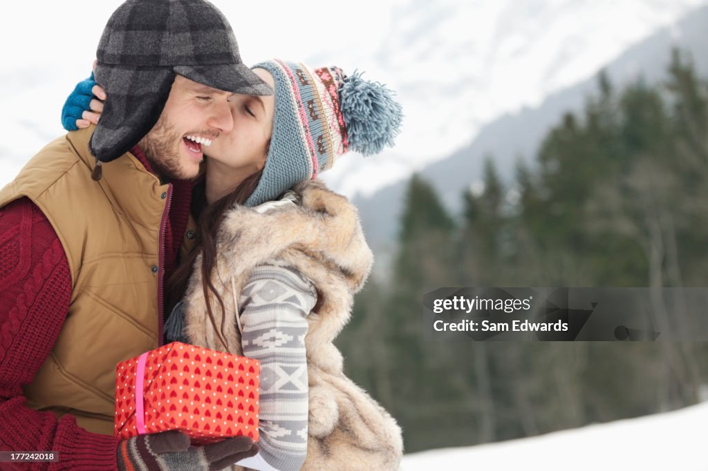 Happy couple with Christmas gift kissing in snowy field