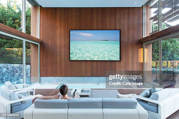 woman watching large flat screen tv in modern living room - tv on wall stock pictures, royalty-free photos & images