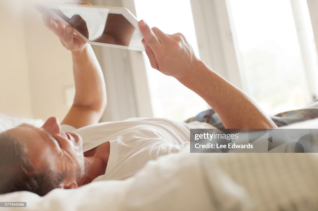 Smiling man laying on bed and using digital tablet