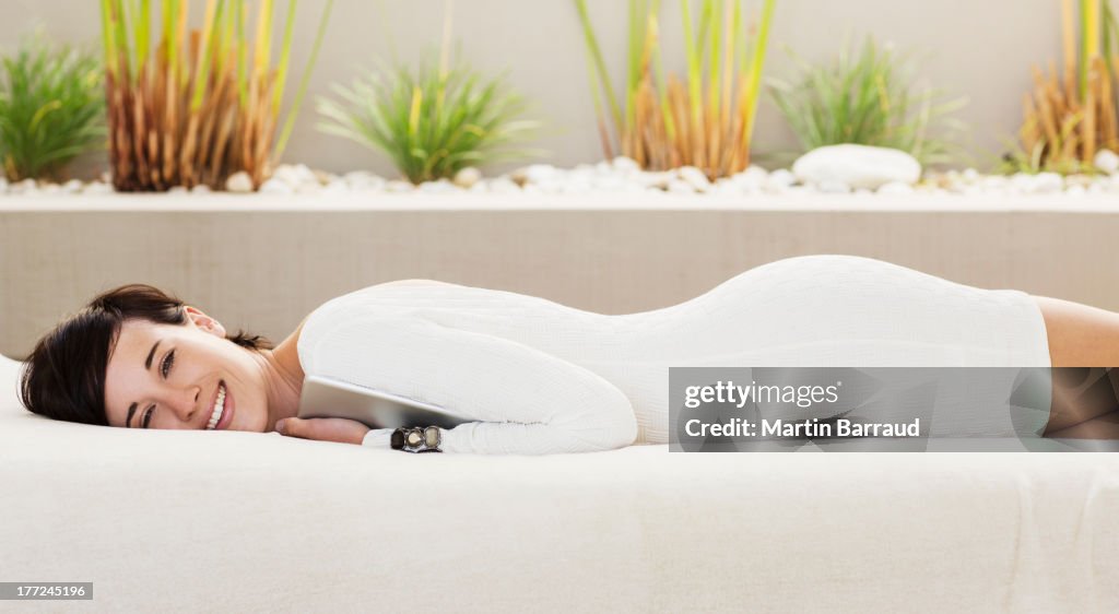 Portrait of smiling woman holding digital tablet and laying on patio sofa