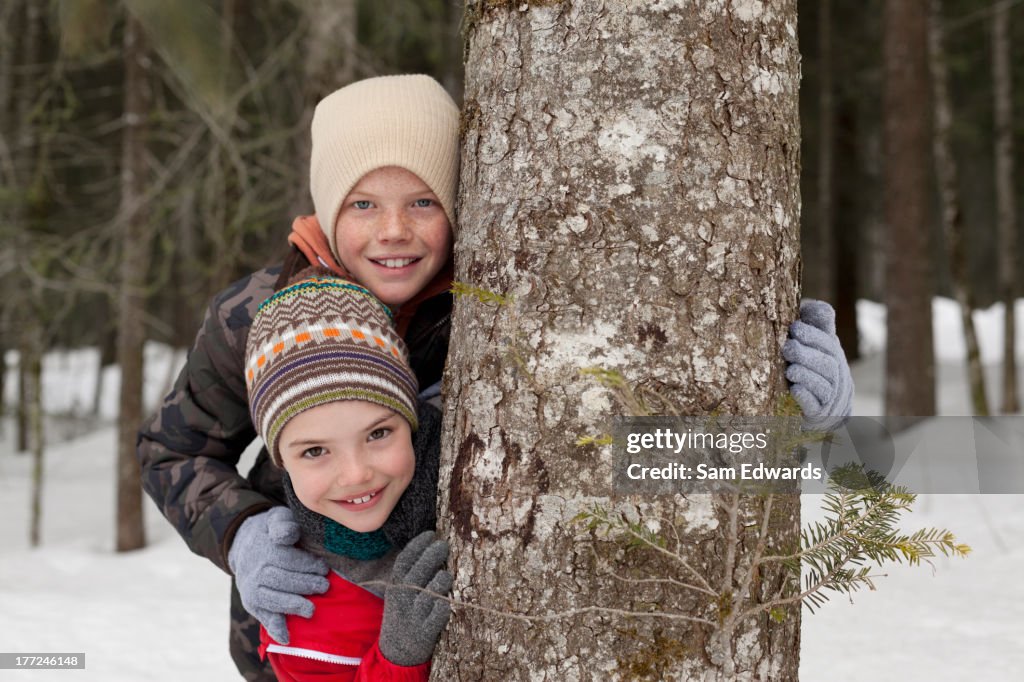 Portrait of happy boys behind tree trunk in snowy woods