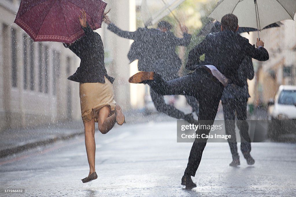 Geschäftsleute mit Sonnenschirmen Tanz im Regen