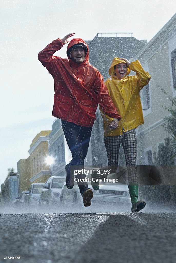 Happy couple in raincoats running down street in rain