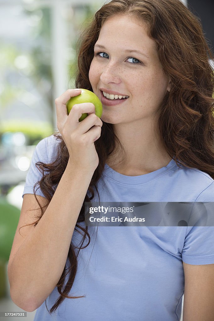 Woman eating a green apple and smiling