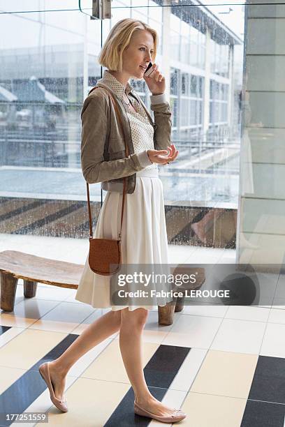 woman talking on a mobile phone while walking on an airport - una mujer de mediana edad solamente fotografías e imágenes de stock