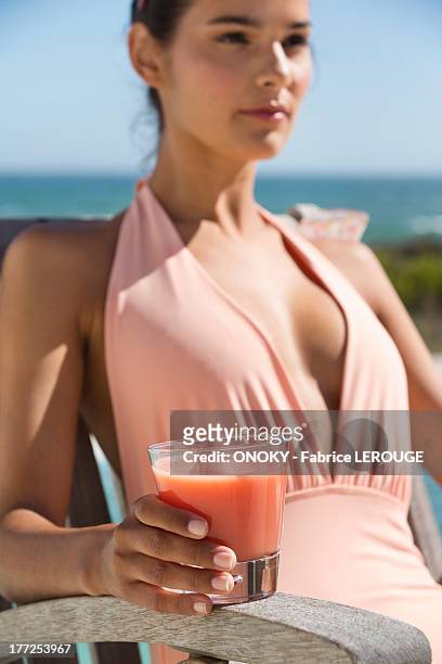 beautiful woman holding a glass of juice and sitting on a chair on the beach - adirondack chair closeup stock pictures, royalty-free photos & images