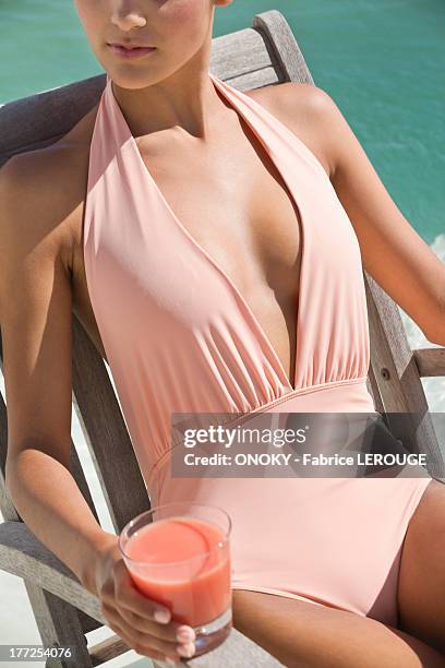 beautiful woman holding a glass of juice and sitting on a chair on the beach - women tanning beach drink stock-fotos und bilder