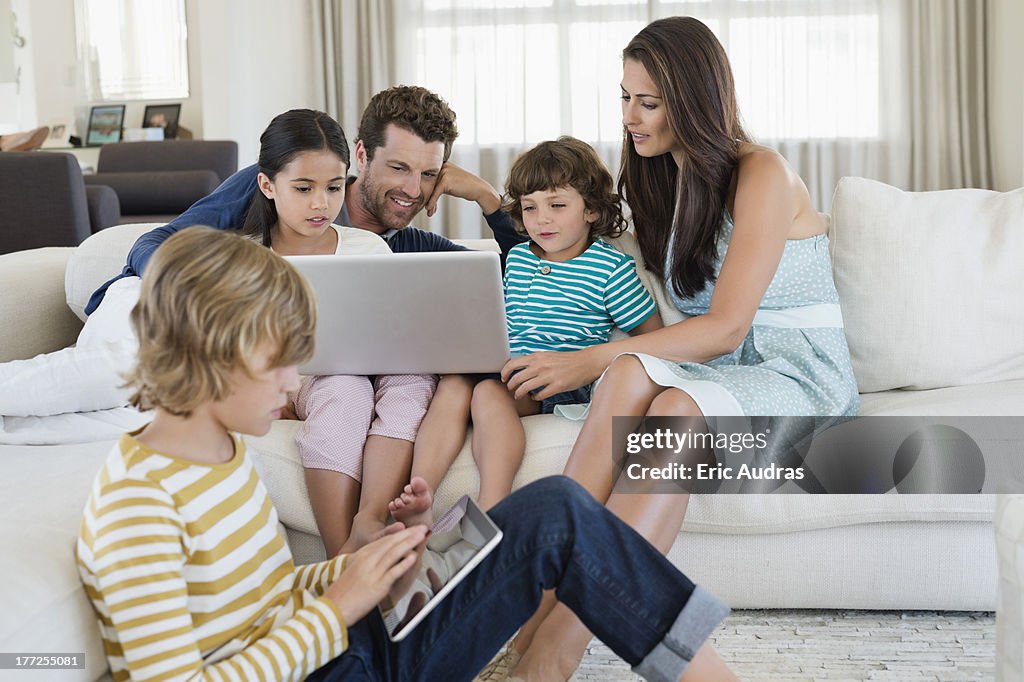 Boy using a digital tablet with his family looking at a laptop