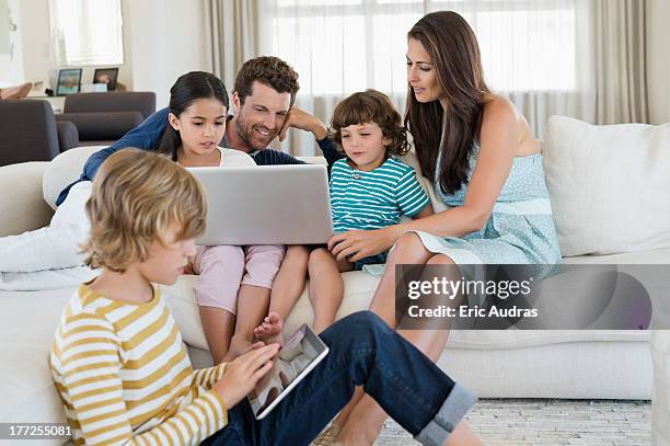 boy using a digital tablet with his family looking at a laptop - famiglia multimediale foto e immagini stock