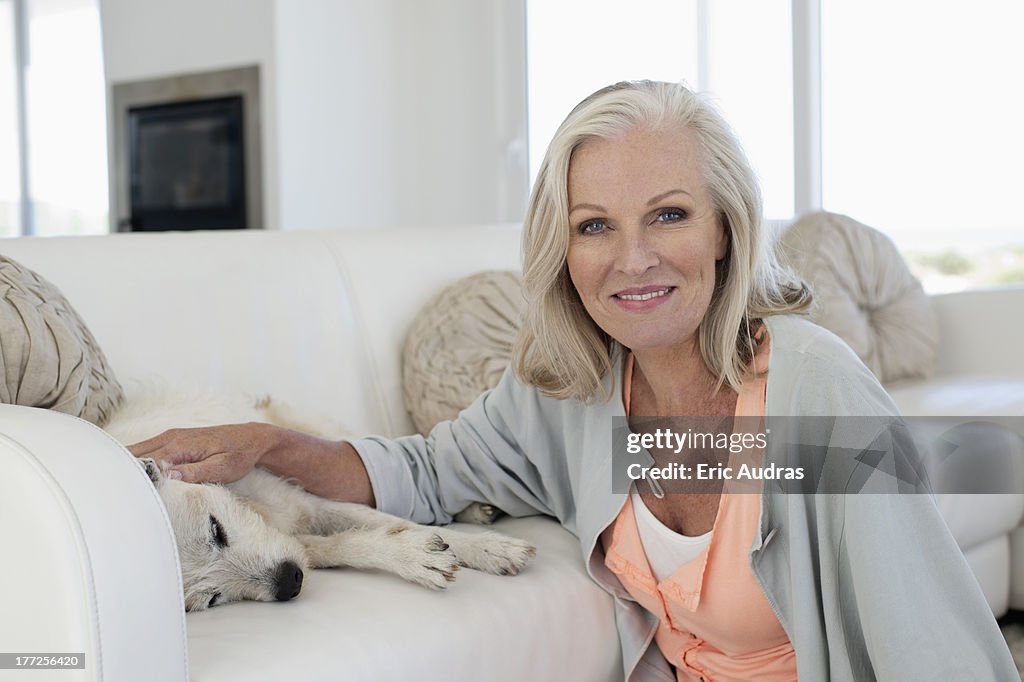 Portrait of a smiling woman stroking her dog lying on couch