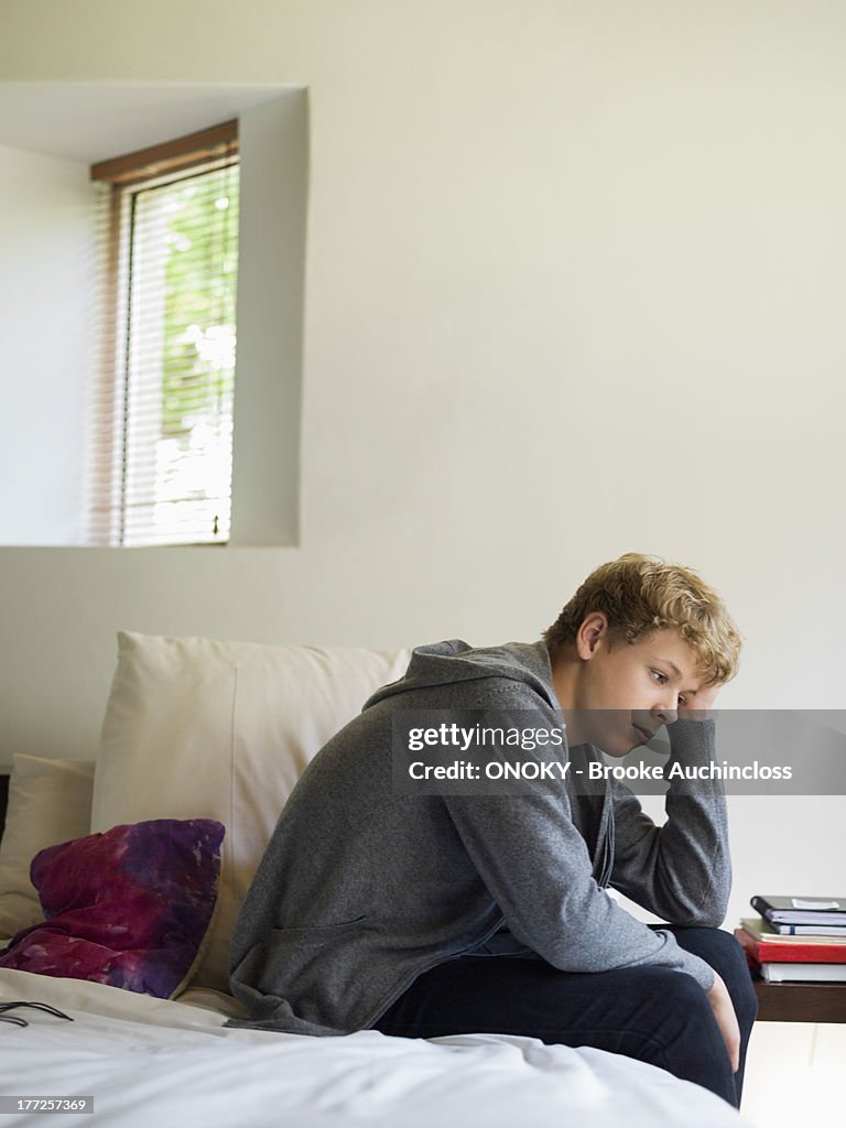 Teenage boy sitting on the bed and thinking