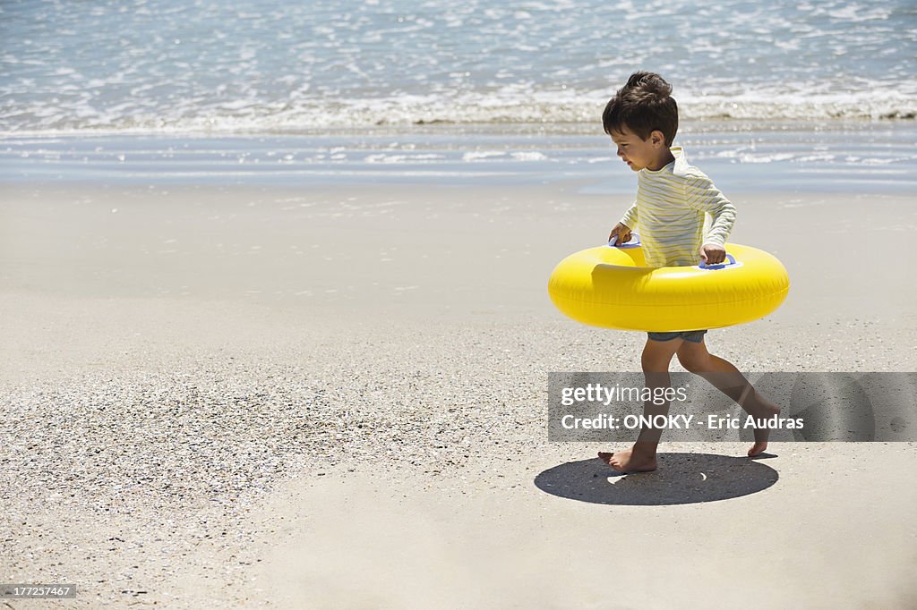 Boy holding an inflatable ring and walking on the beach