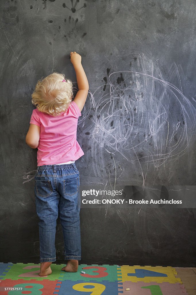 Rear view of a girl writing on a blackboard