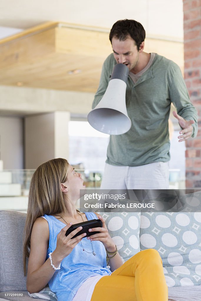 Man shouting into a megaphone at his daughter for playing video game