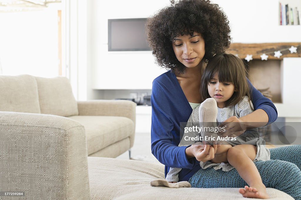 Woman putting on socks to her daughter and smiling