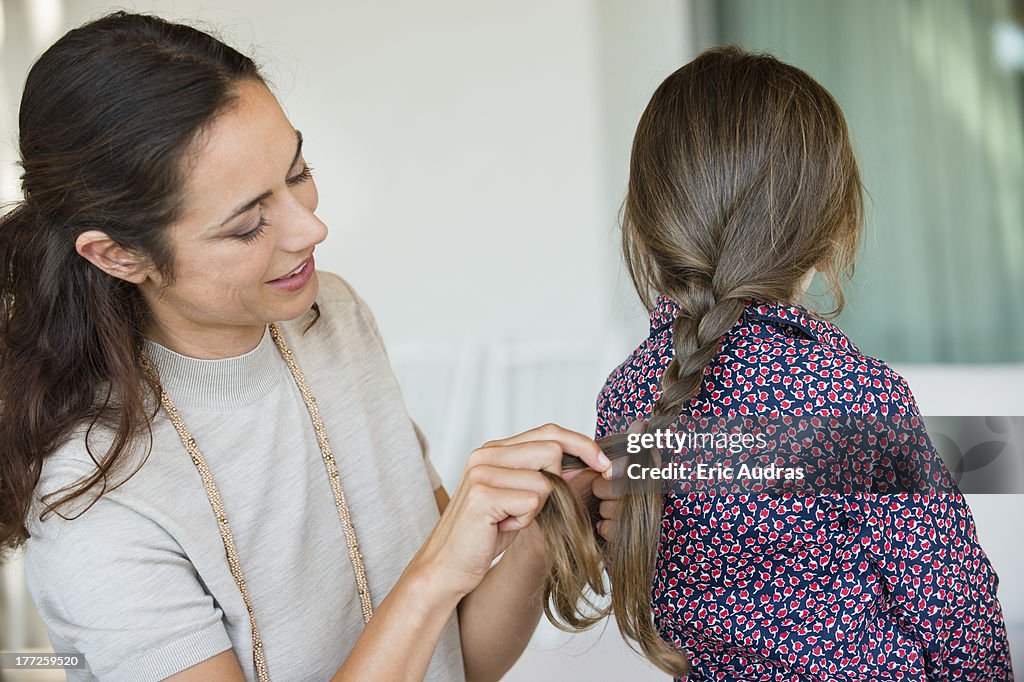 Smiling woman braiding her daughter's hair