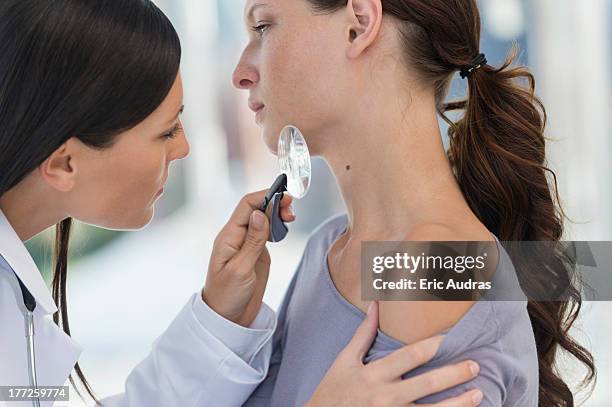 dermatologist using magnifying glass to examine woman's skin - dermatology stock pictures, royalty-free photos & images