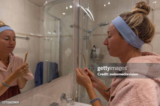 frau, die ihre zunge im spiegel putzt, persönliche hygiene - mundspülung stock-fotos und bilder