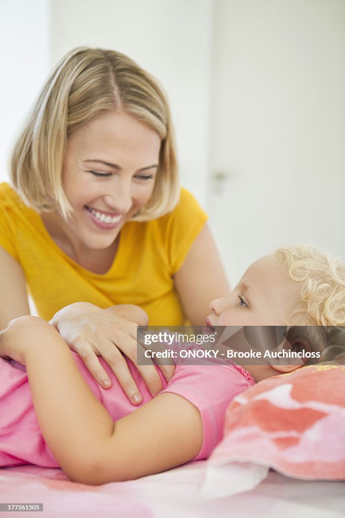 Smiling woman looking at her daughter lying on the bed