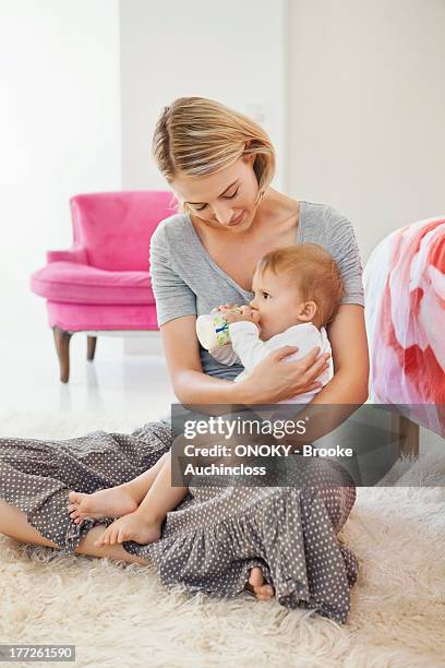 woman sitting with her baby feeding with a baby bottle - donne bionde scalze foto e immagini stock