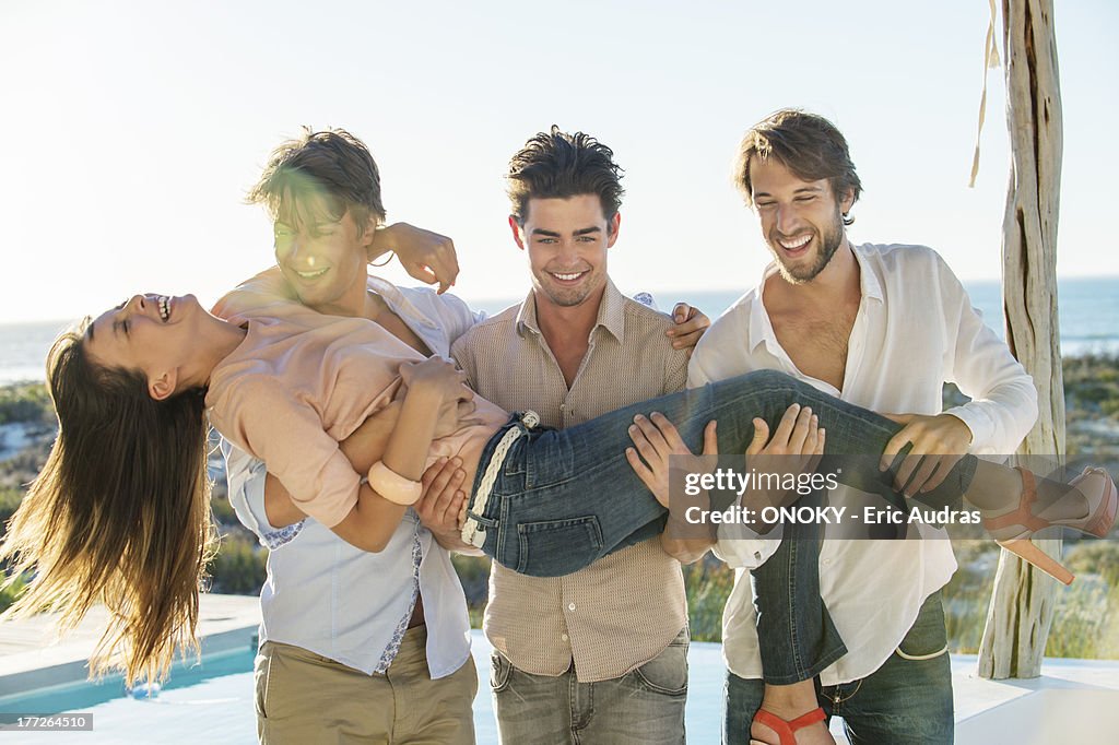 Three men lifting their female friend at the poolside