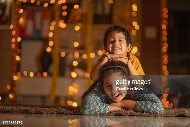 glückliche geschwister, die zu hause auf dem teppich liegen - diwali family stock-fotos und bilder
