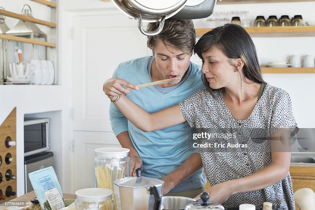 Woman tasting food to her husband in the kitchen