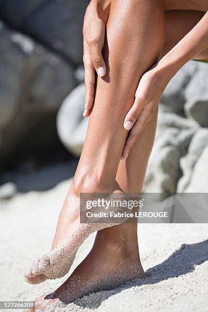 woman applying suntan lotion on her leg on the beach - womens beautiful feet - fotografias e filmes do acervo